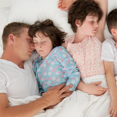 Eltern schlafen mit drei Kindern in einem Bett.