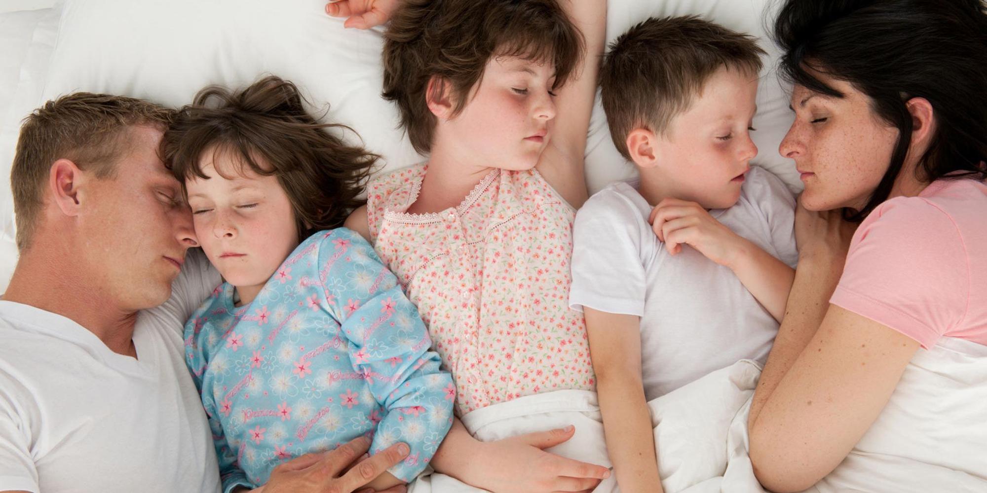 Eltern schlafen mit drei Kindern in einem Bett.