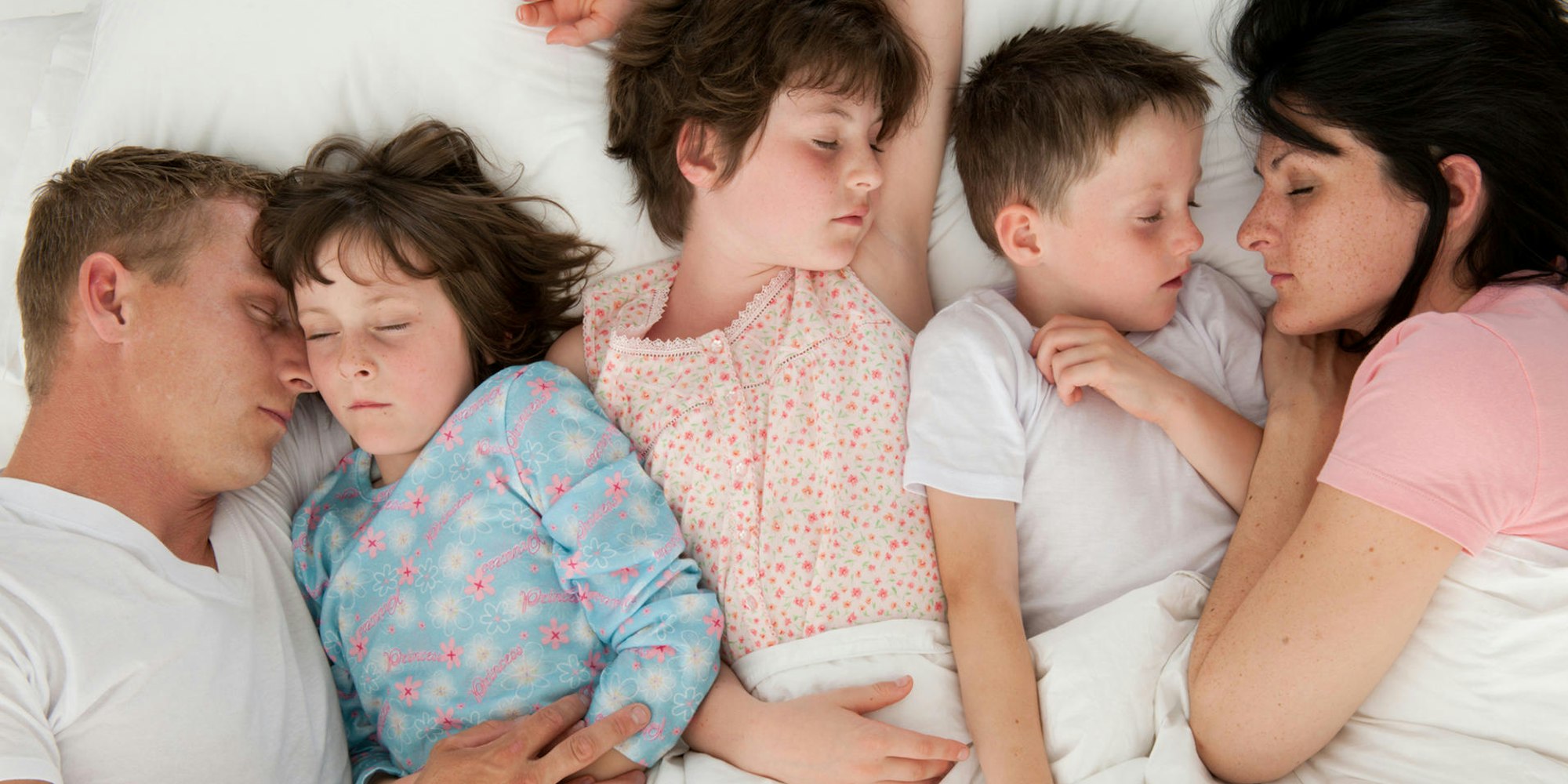 Eltern schlafen mit drei Kindern in einem Bett.