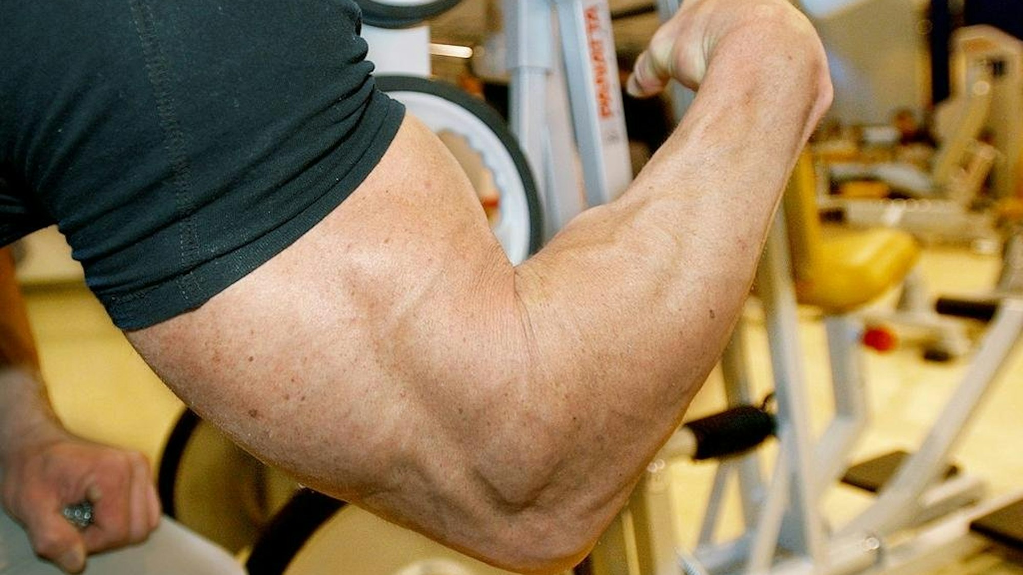 Ein Mann zeigt seinen sehr großen Bizeps unter einem aufgerollten T-Shirt.