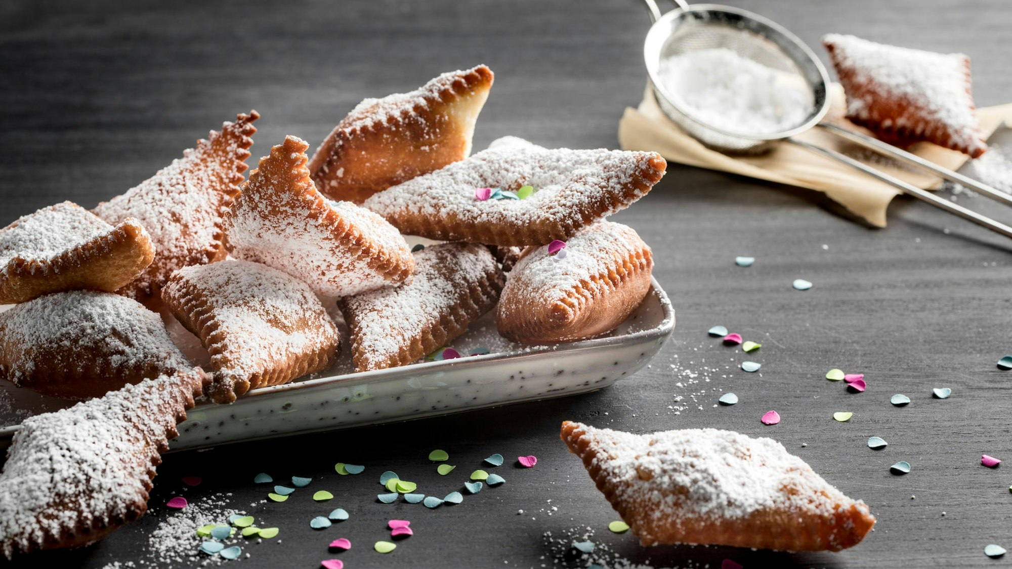 Puderzuckerbestäubte Muzen liegen in einem Schälchen angerichtet, Konfetti liegt drumherum