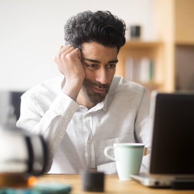 Mann sitzt müde und demotiviert vor seinem Laptop