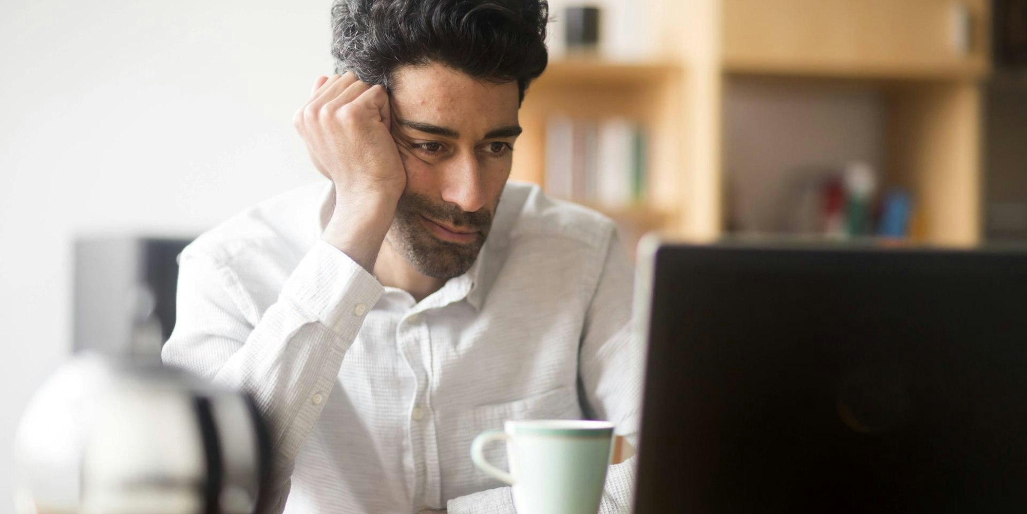 Mann sitzt müde und demotiviert vor seinem Laptop