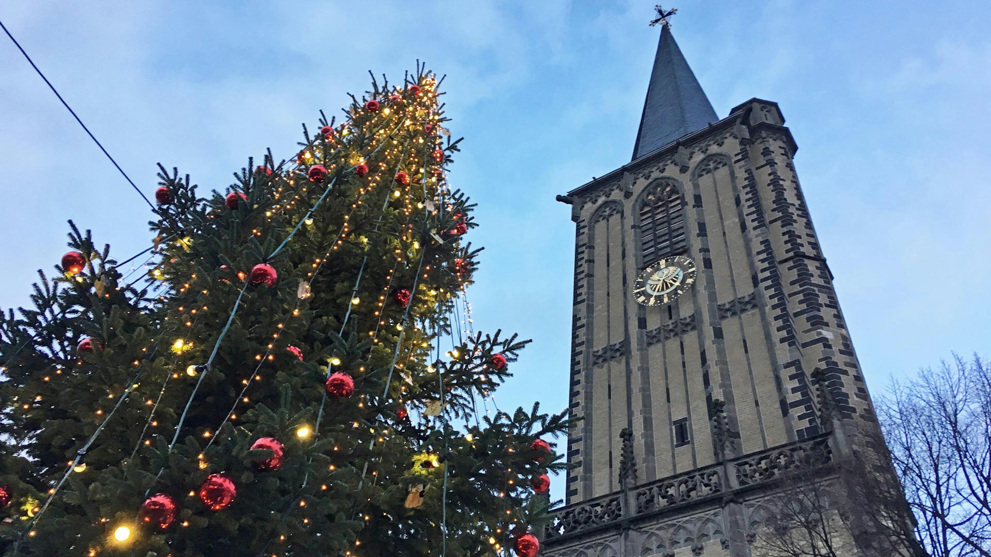 Kirchturm ragt in den Himmel, daneben ein geschmückter Weihnachtsbaum