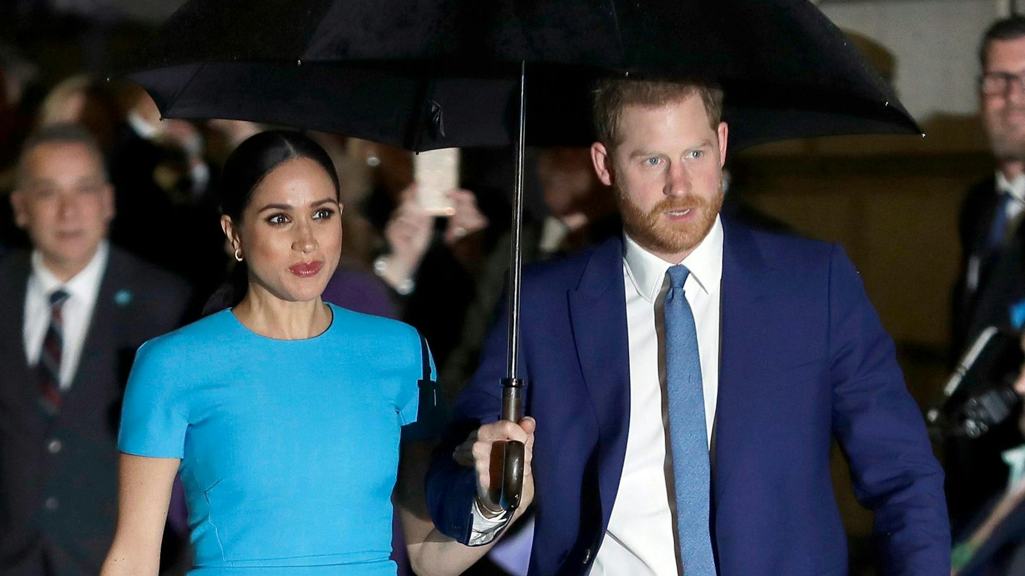 Herzogin Meghan und Prinz Harry laufen unter einem Regenschirm.