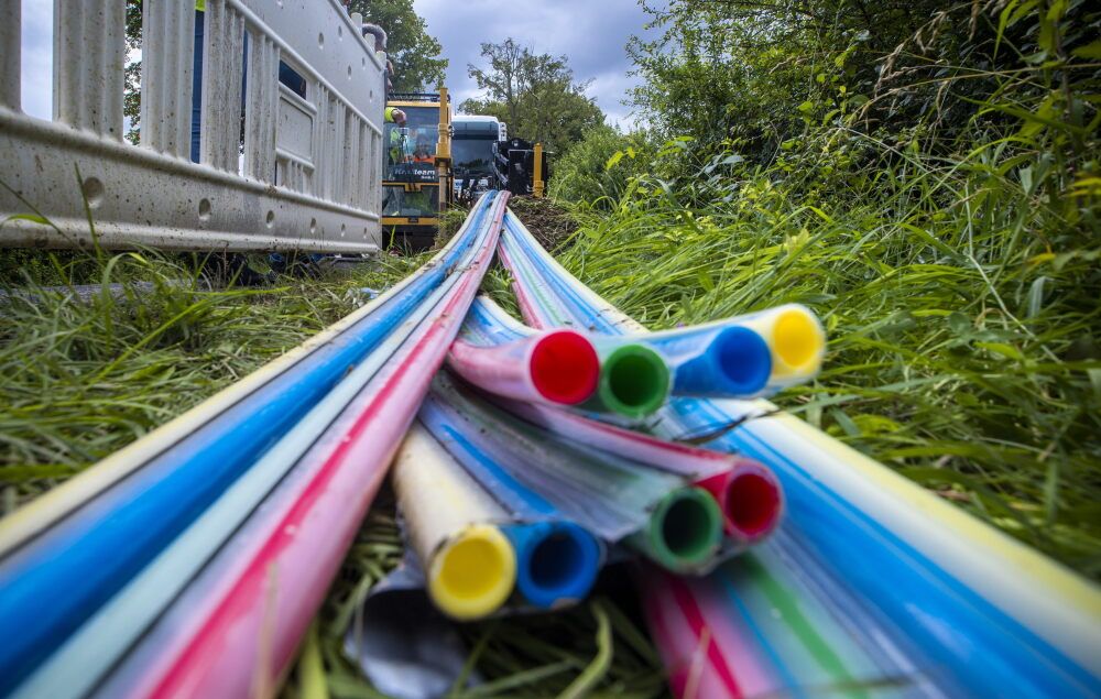 Bunte Kabelhülsen liegen im Gras, im Hintergrund stehen Bagger.