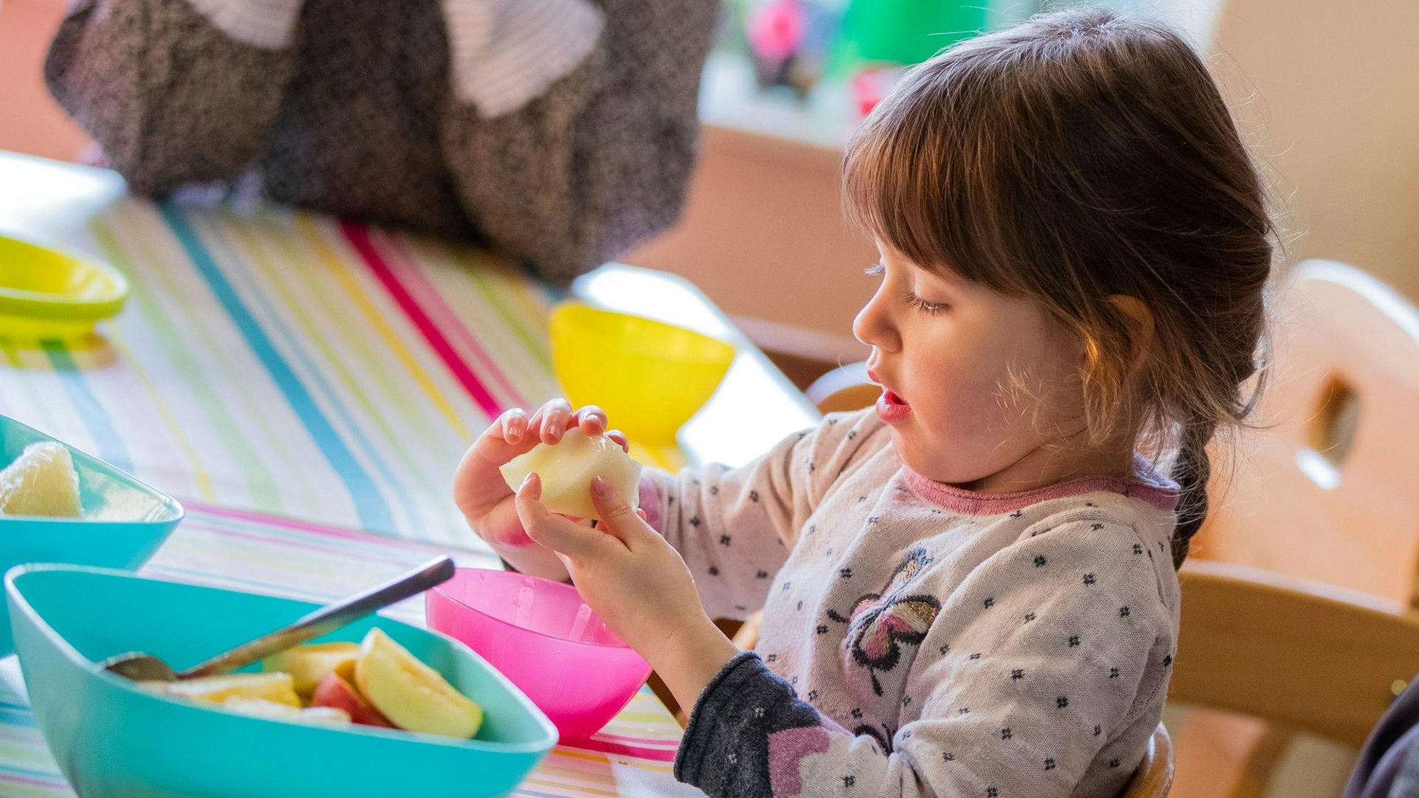 Ein Mädchen sitzt am Tisch einer Tagesmutter und isst Obst.