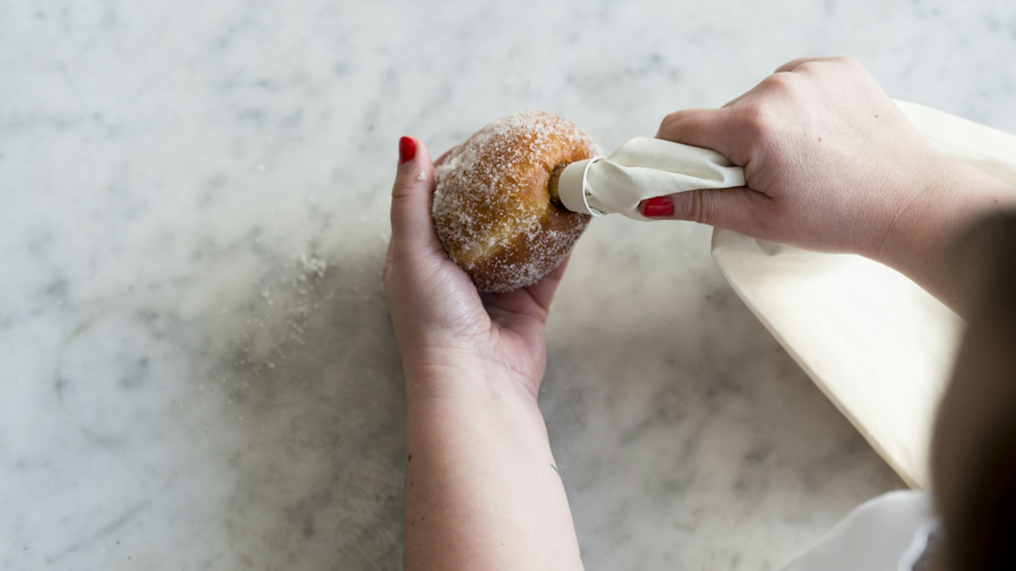 Ein Berliner wird mit einer Spritztüte gefüllt.
