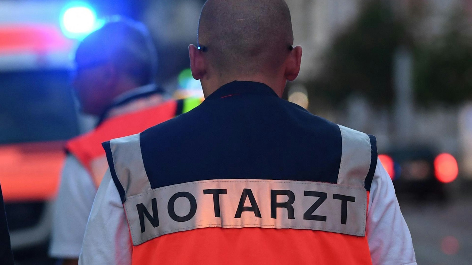 Ein Notarzt mit einer Weste steht an einem Unfallort.