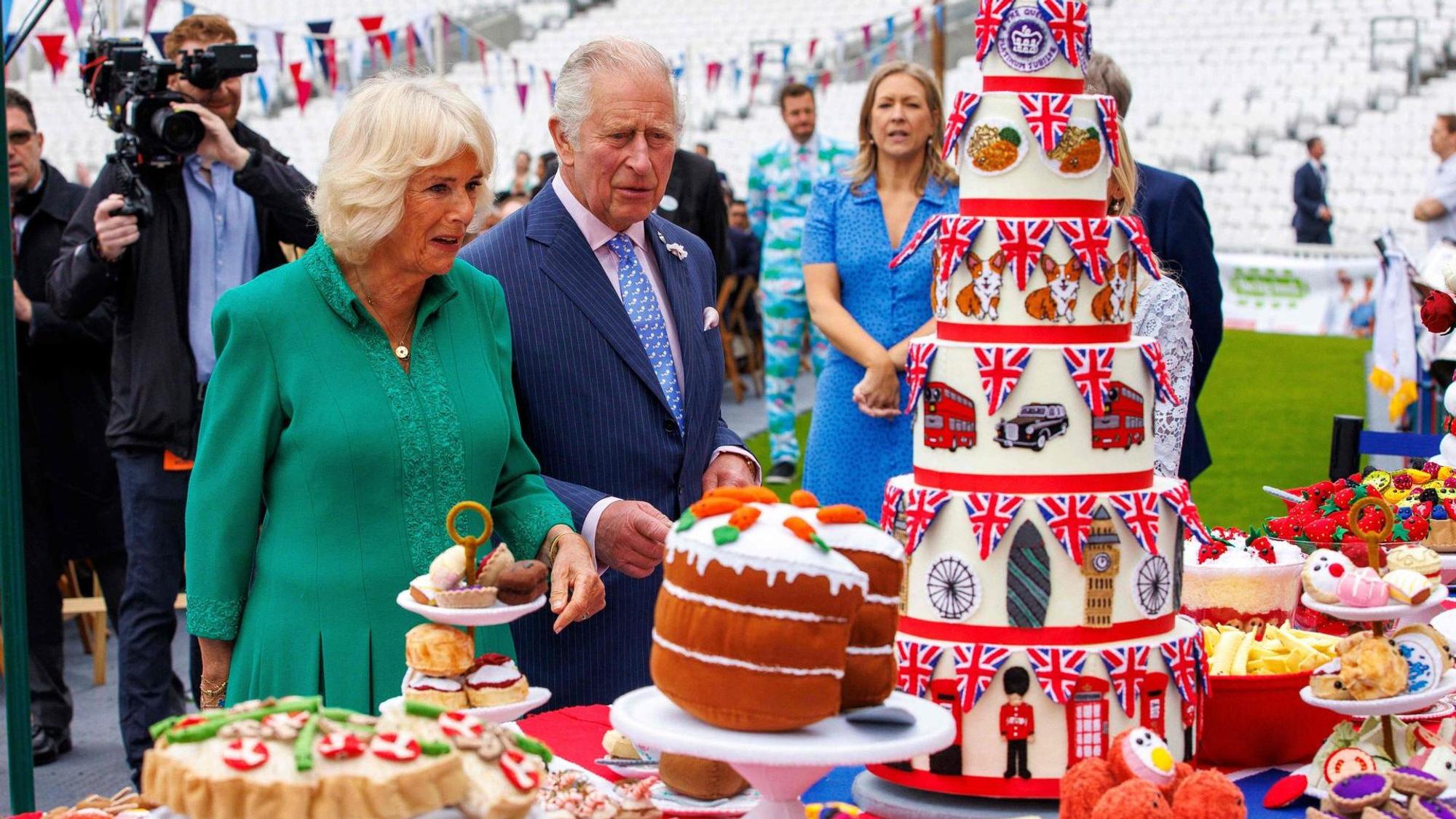 Königin Camilla und König Charles stehen vor einem Tisch mit reich verziertem Gebäck, Kuchen und Torten.