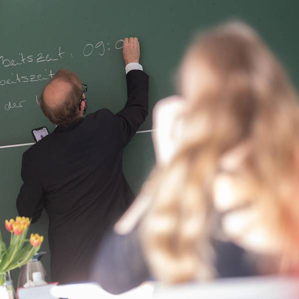 Ein Lehrer schreibt etwas an die Tafel.