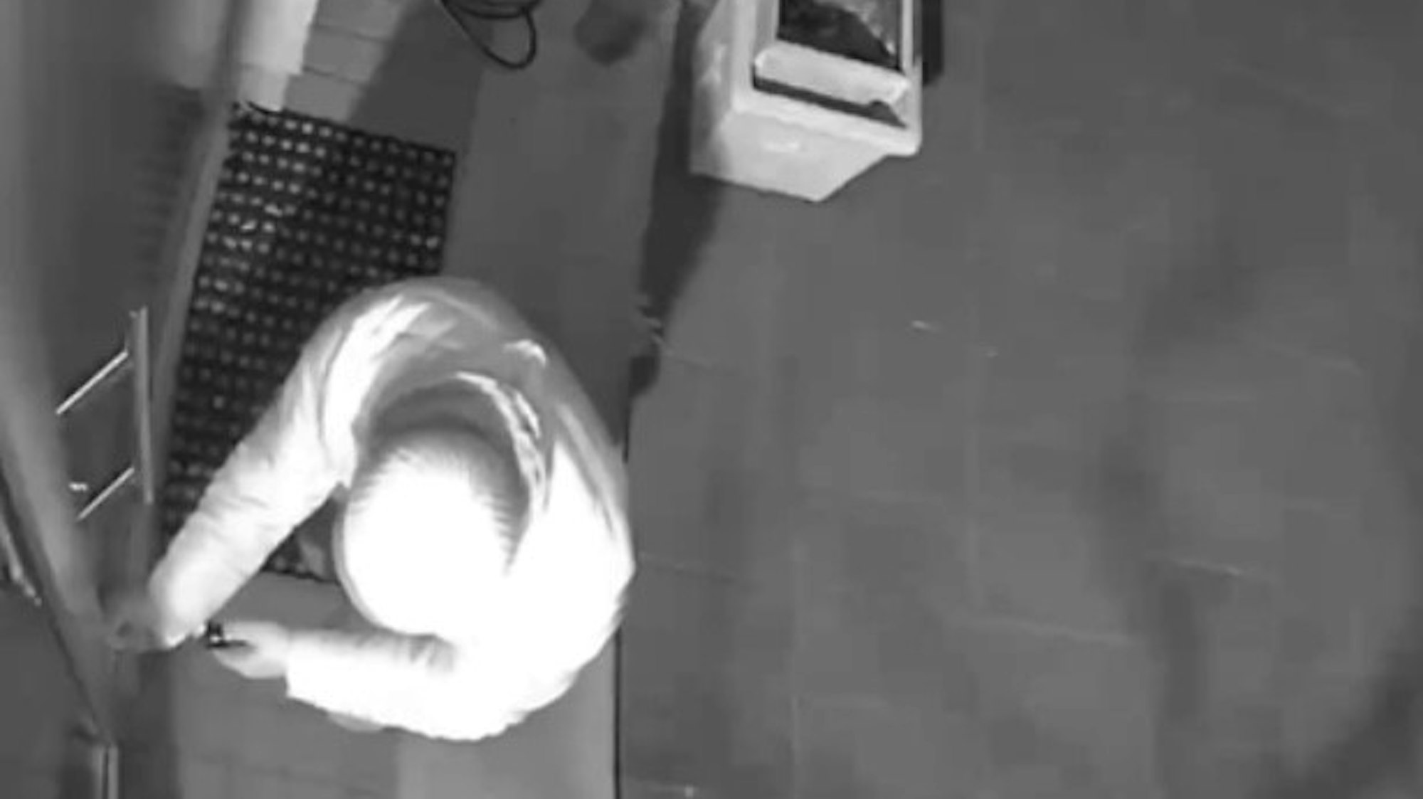 Ein hell gekleideter Einbrecher mit Mütze macht sich an einer Haustür zu schaffen.