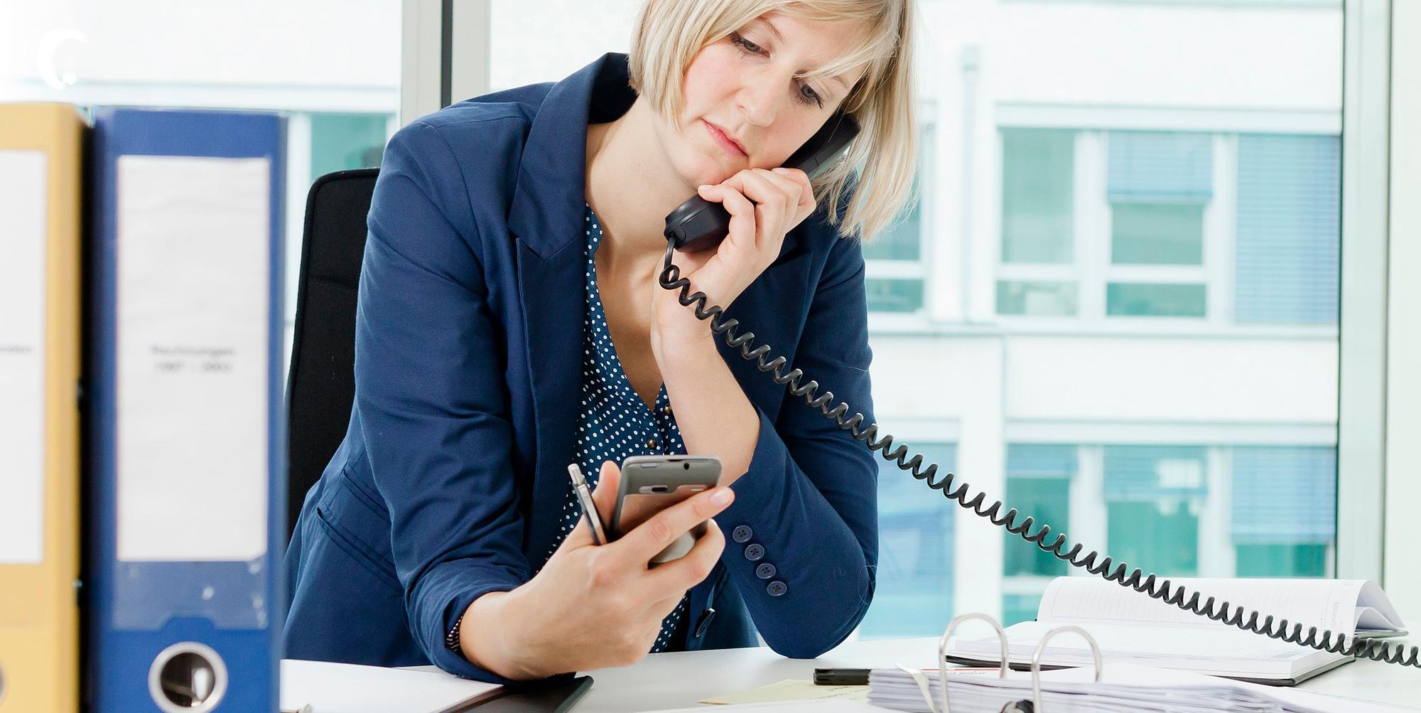 Frau im Büro guckt auf Handy