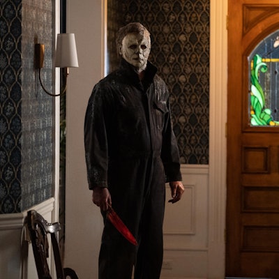 Die Hauptfigur der Halloween-Serie mit einem blutverschmiertem Messer steht im Flur eines Hauses. Er trägt seine berühmte, weiße Maske.