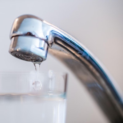 Wasser tropft aus einem Hahn in ein Glas.