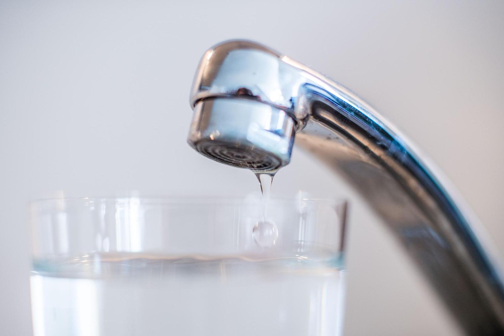 Wasser tropft aus einem Hahn in ein Glas.