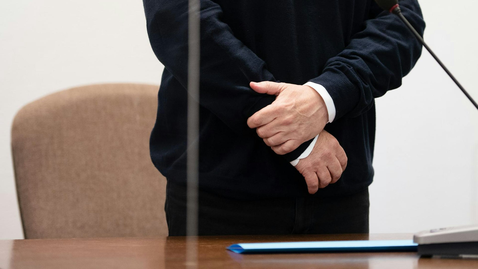 Mit verschränkten Armen steht der Angeklagte vor seinem Stuhl.