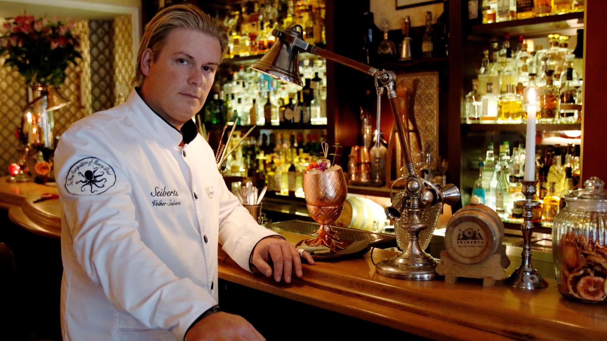 Mann in weißer Jacke steht am Tresen einer Bar