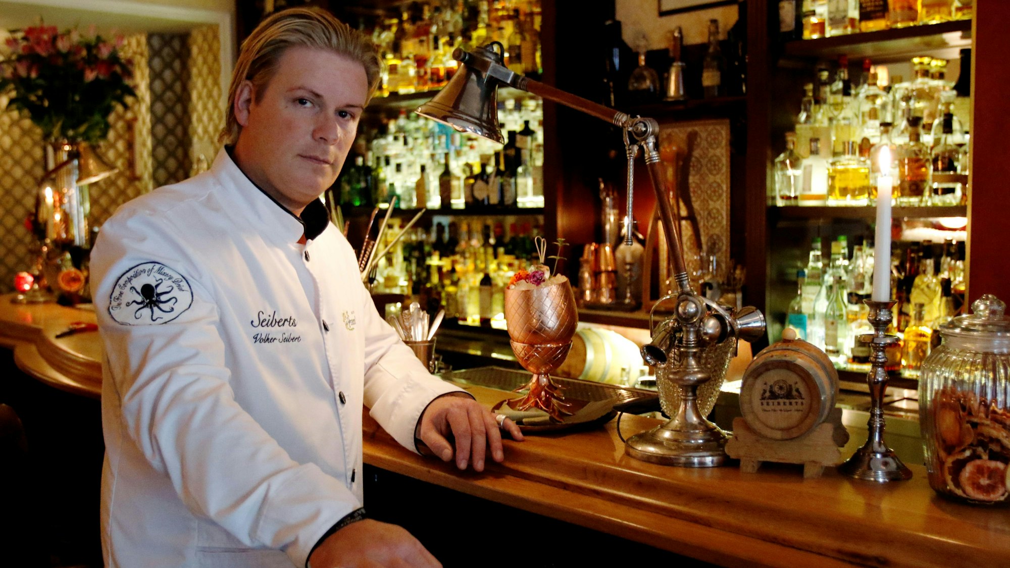 Mann in weißer Jacke steht am Tresen einer Bar