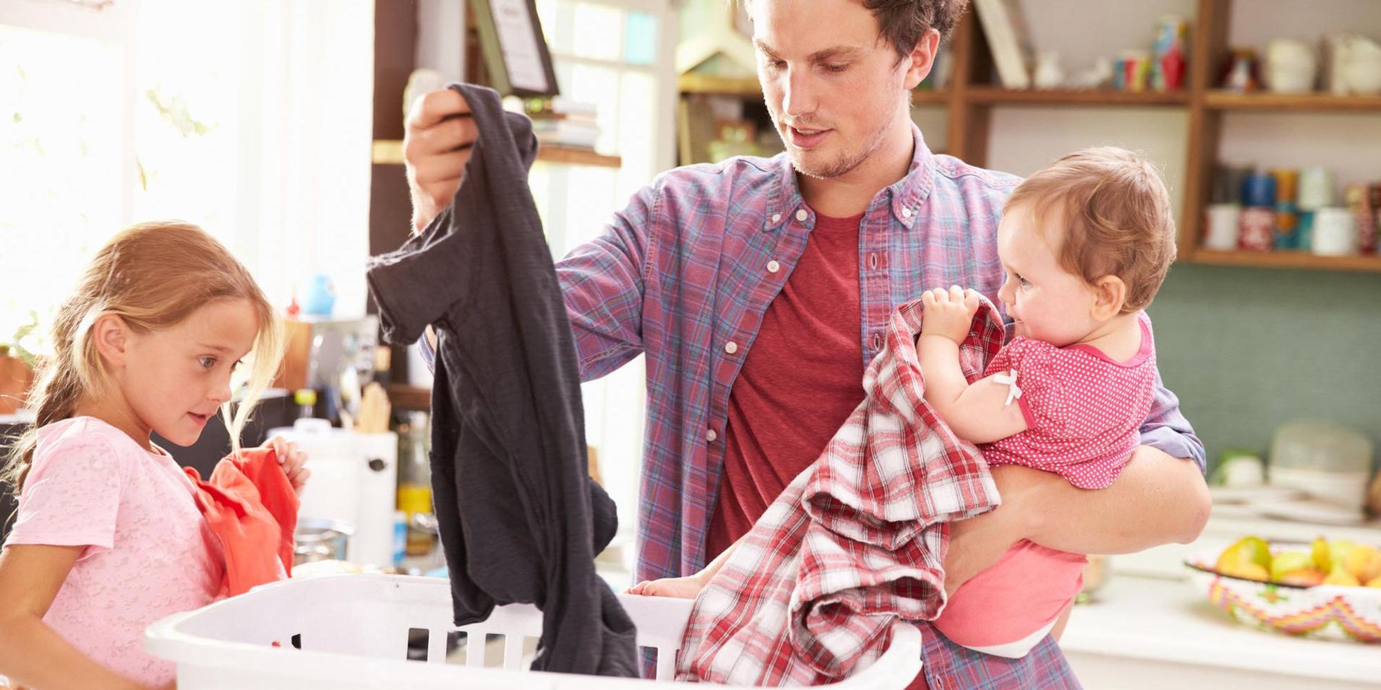 Ein Vater macht die Wäsche mit einem Baby auf dem Arm.