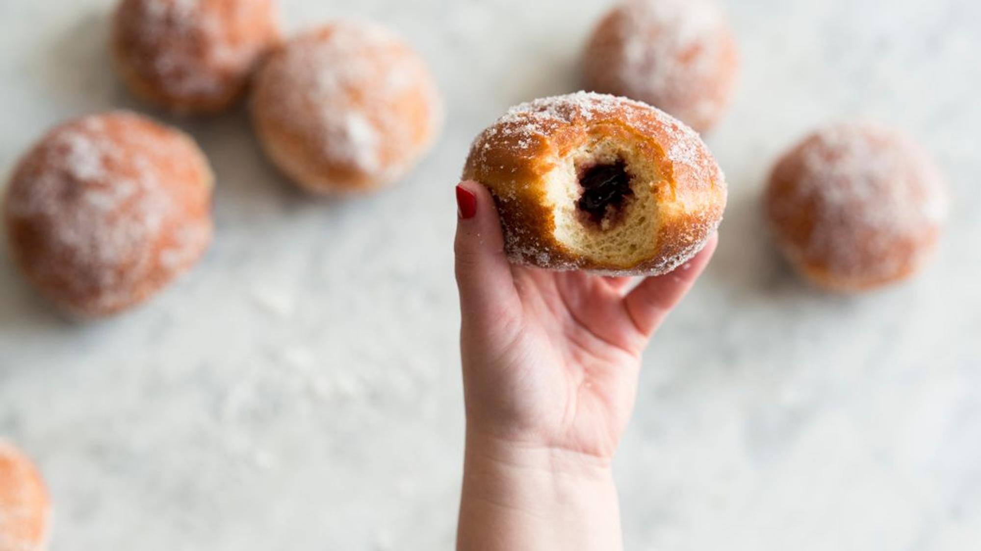 Ein angebissener Berliner wird in die Kamera gehalten, sodass die Füllung zu sehen ist.