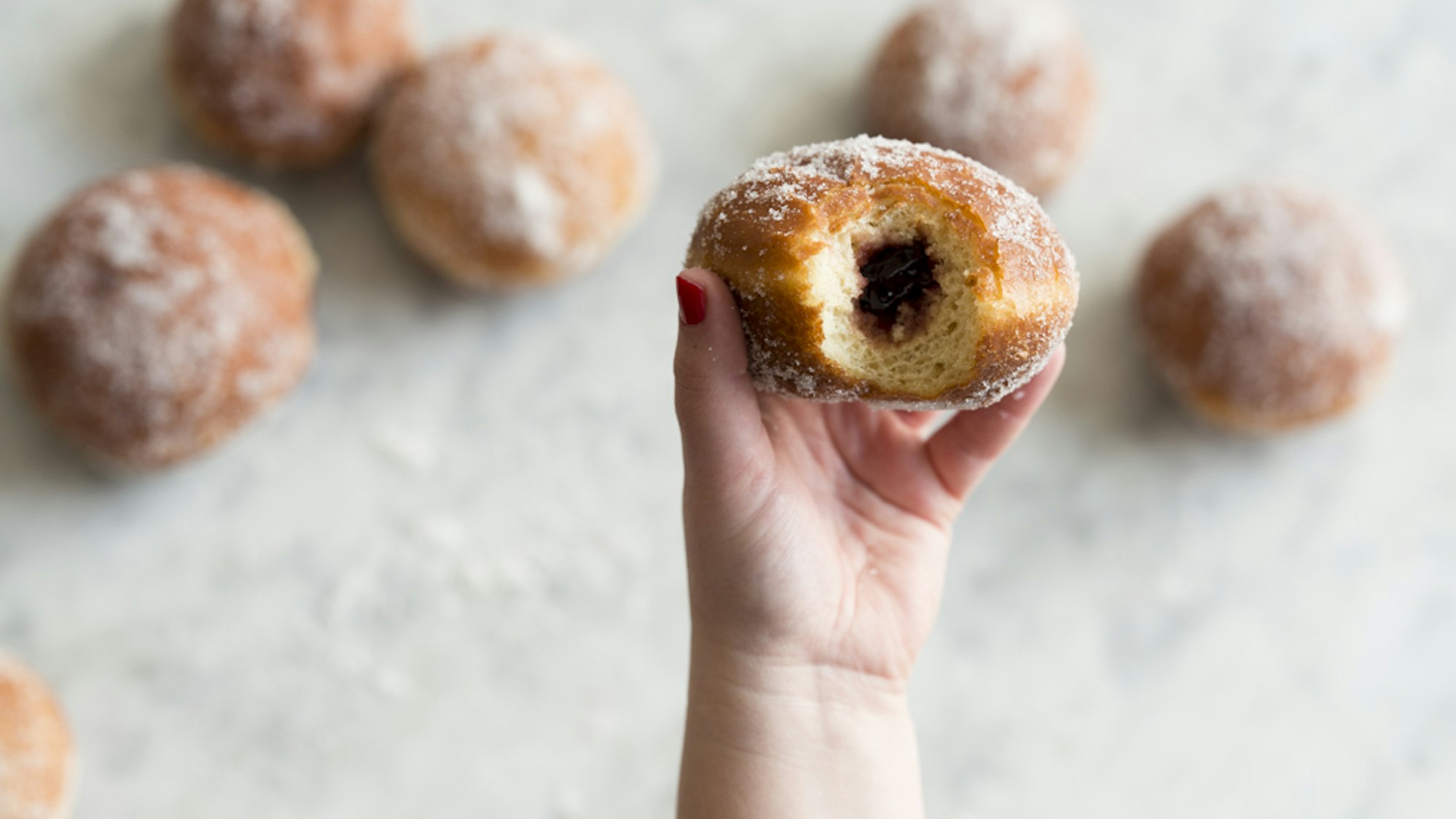Ein angebissener Berliner wird in die Kamera gehalten, sodass die Füllung zu sehen ist.