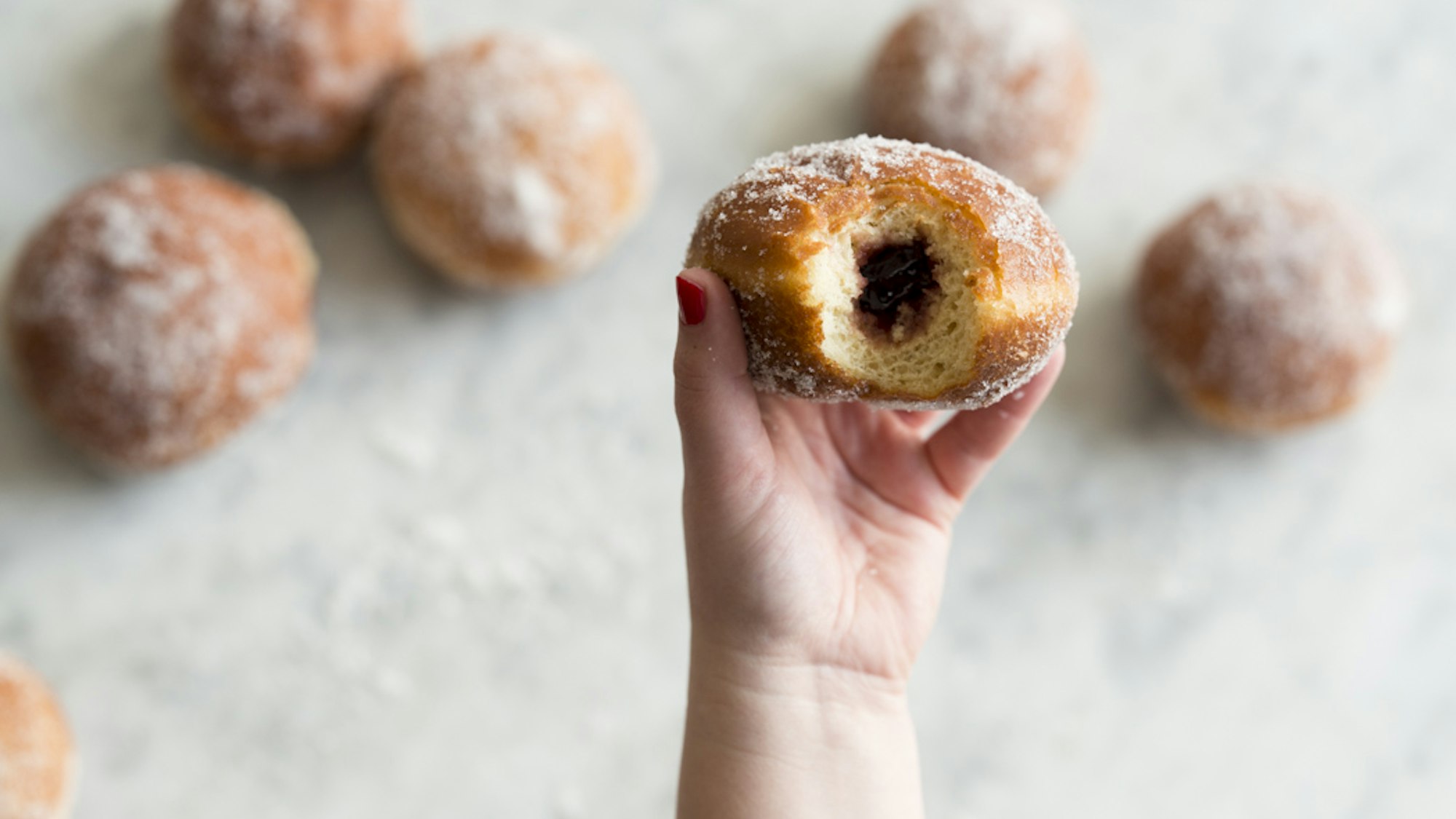 Ein angebissener Berliner wird in die Kamera gehalten, sodass die Füllung zu sehen ist.