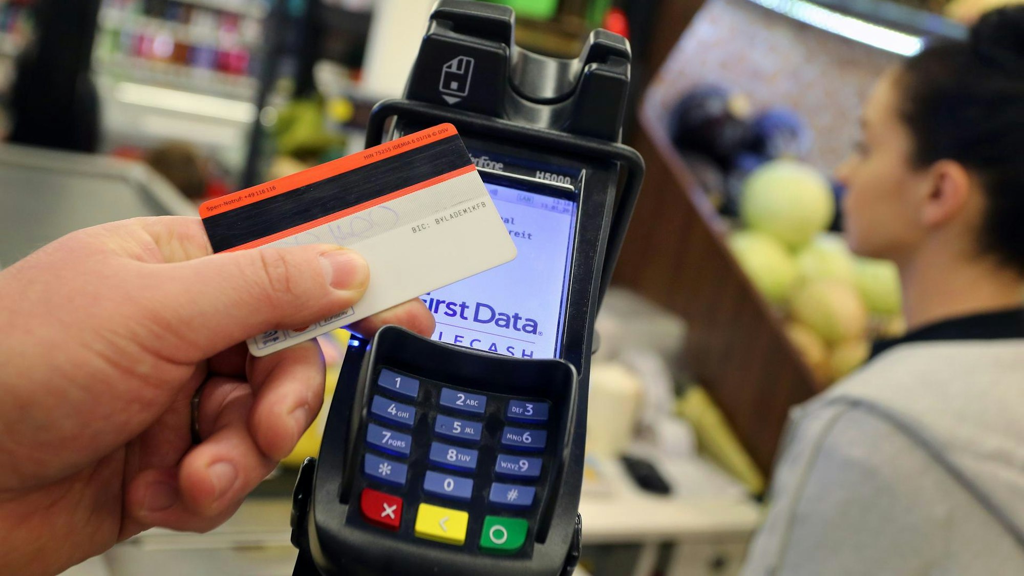 Eine Hand hält eine EC-Karte an das Kartenlesegerät.