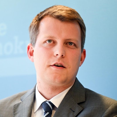 Henning Höne spricht bei einer Veranstaltung. Er ist im Porträt zu sehen vor einer hellblauen FDP-Werbewand.