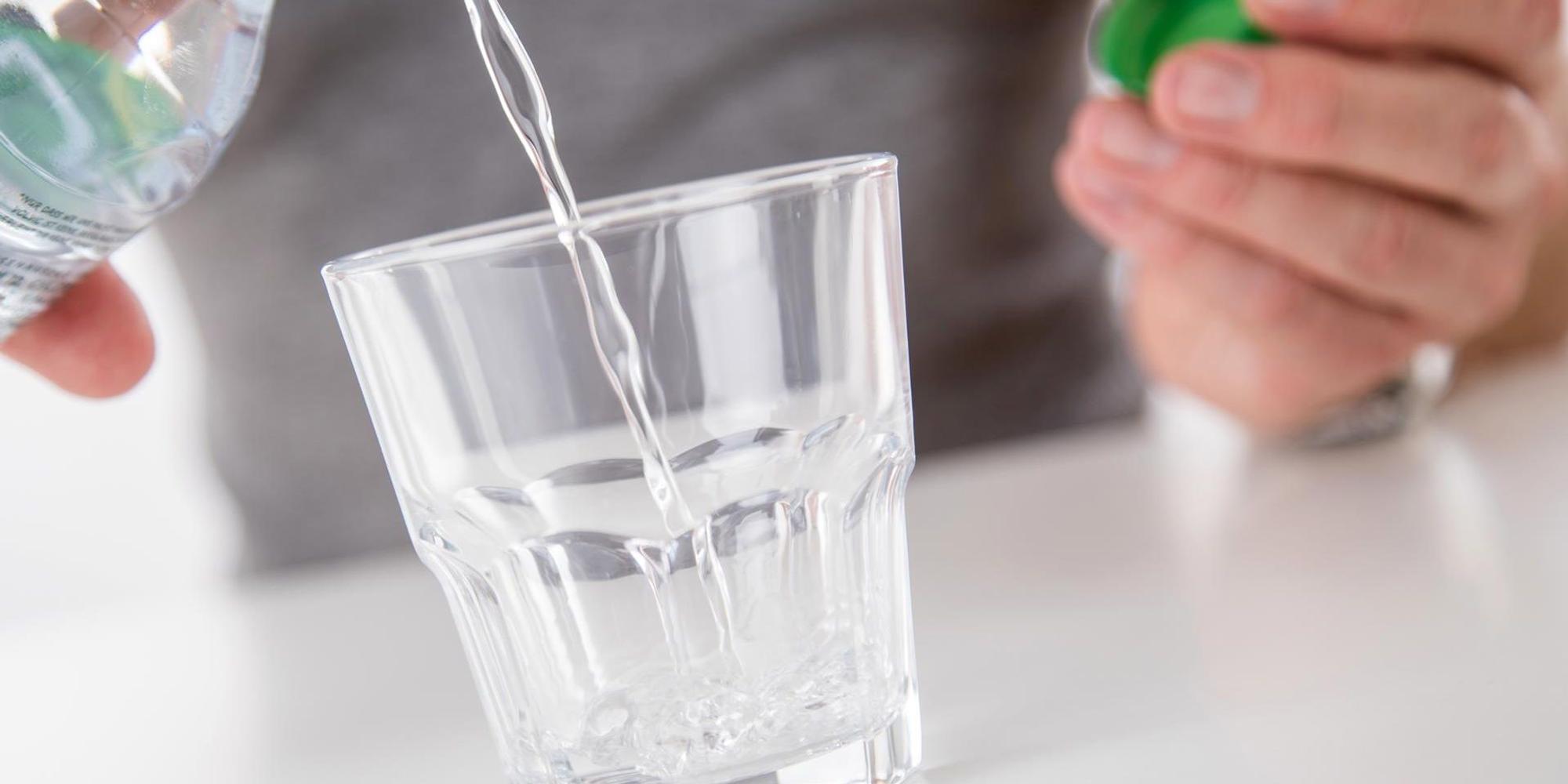 Jemand schüttet sich ein Glas Mineralwasser ein