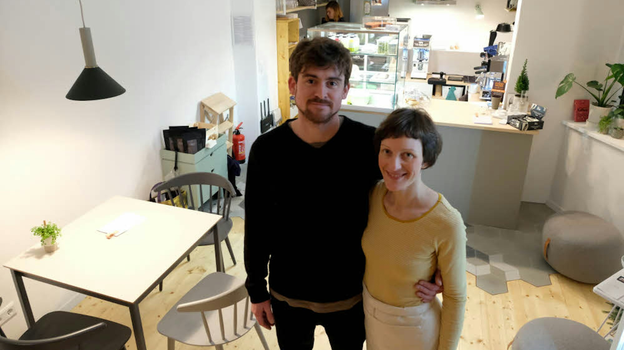Sarah Hoven-Lambertz steht Arm in Arm mit ihrem Mann Niko Lambertz in ihrem Café Südlicht in Köln.
