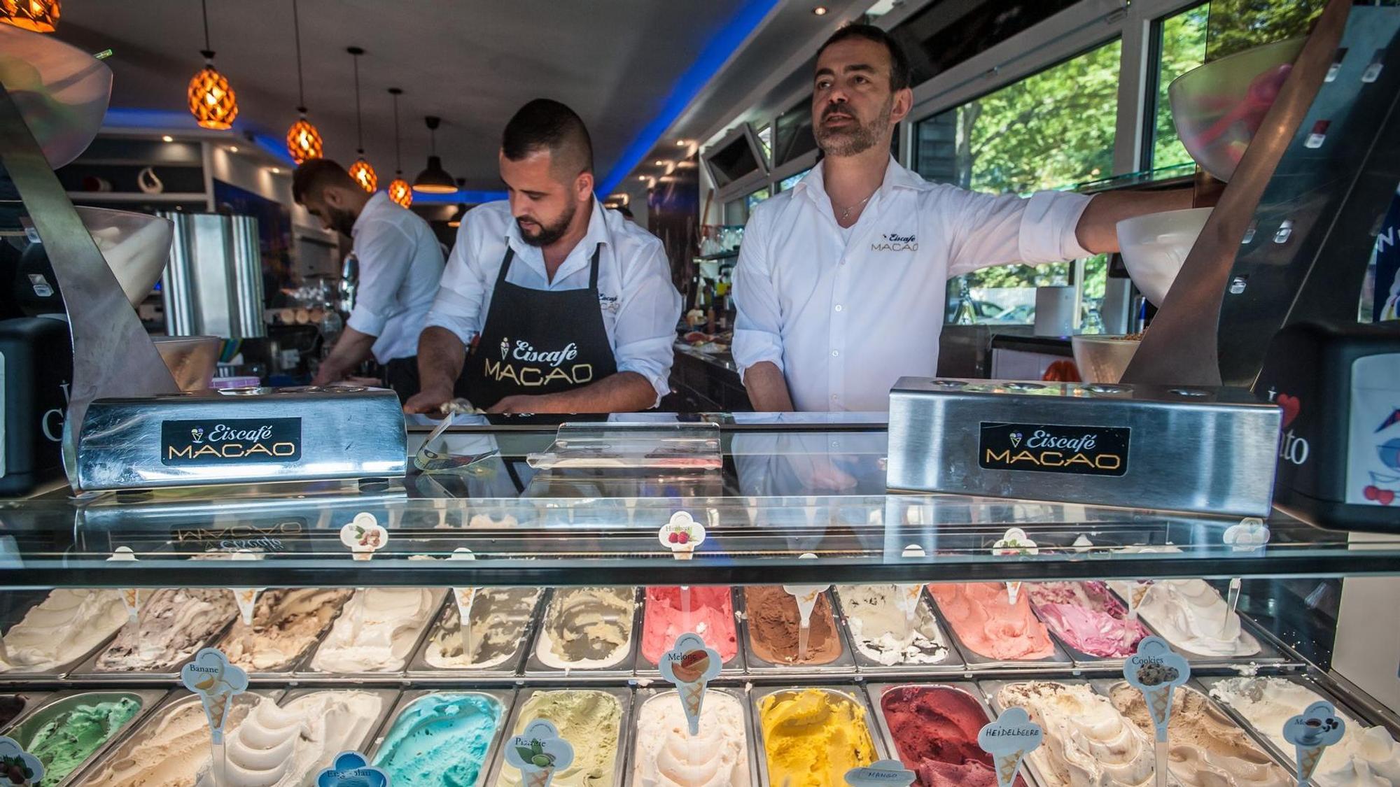 Hinter der Eistheke der Eisdiele Macao arbeiten mehrere Männer, im Vordergrund sind Eissorten zu sehen.