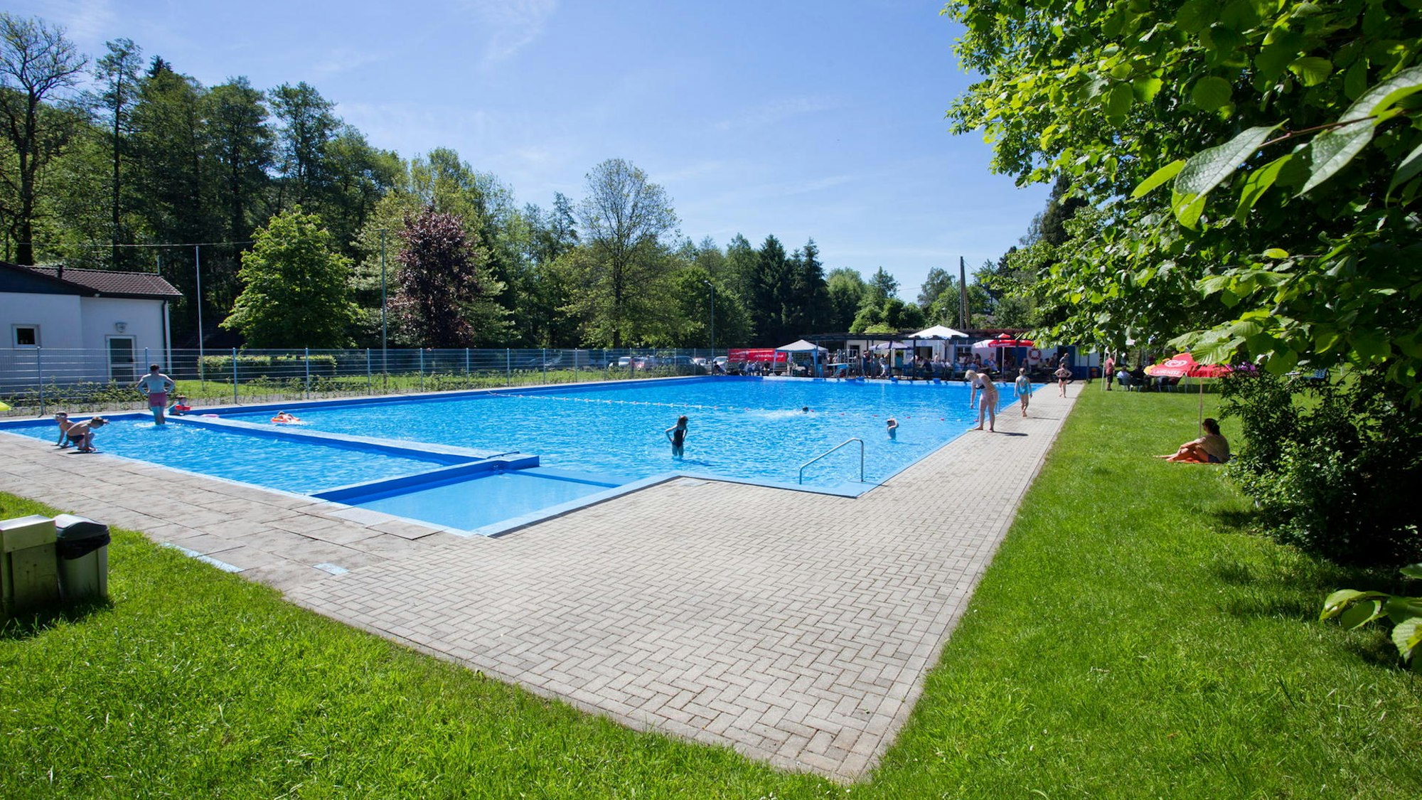Ein Freibad mit einem großen Becken, in dem wenige Leute schwimmen.