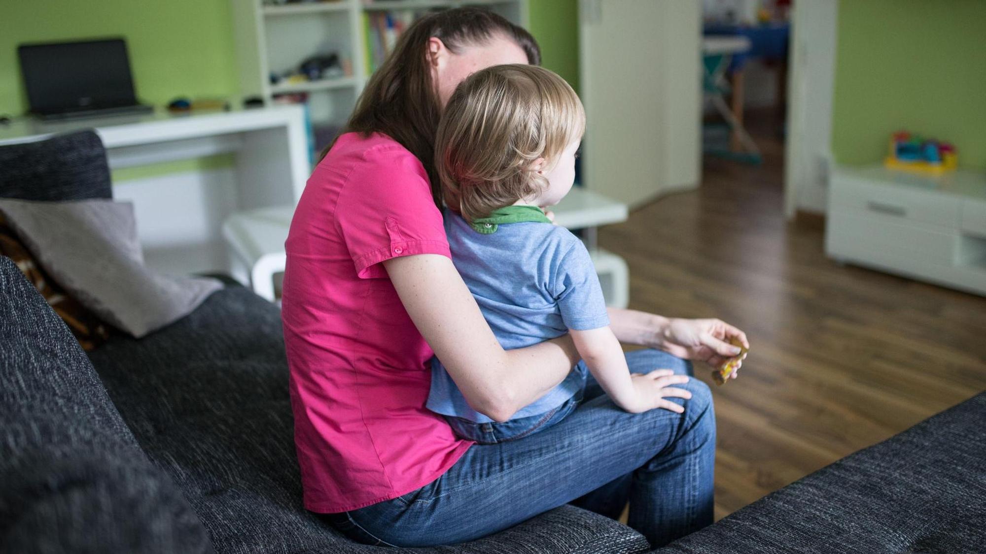 Eine Frau sitzt im Wohnzimmer und hält ein kleines Kind auf dem Schoß.