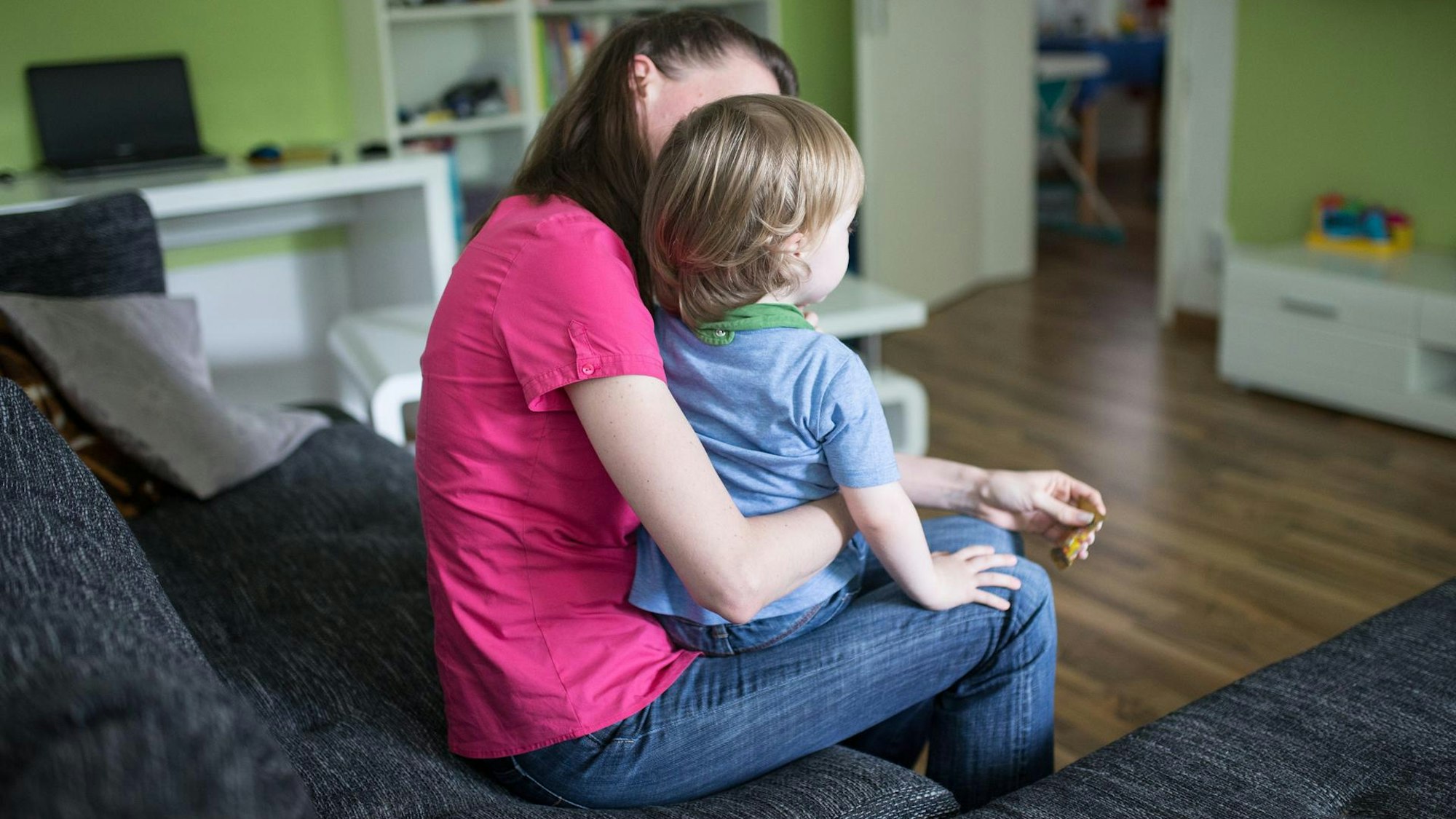 Eine Frau sitzt im Wohnzimmer und hält ein kleines Kind auf dem Schoß.