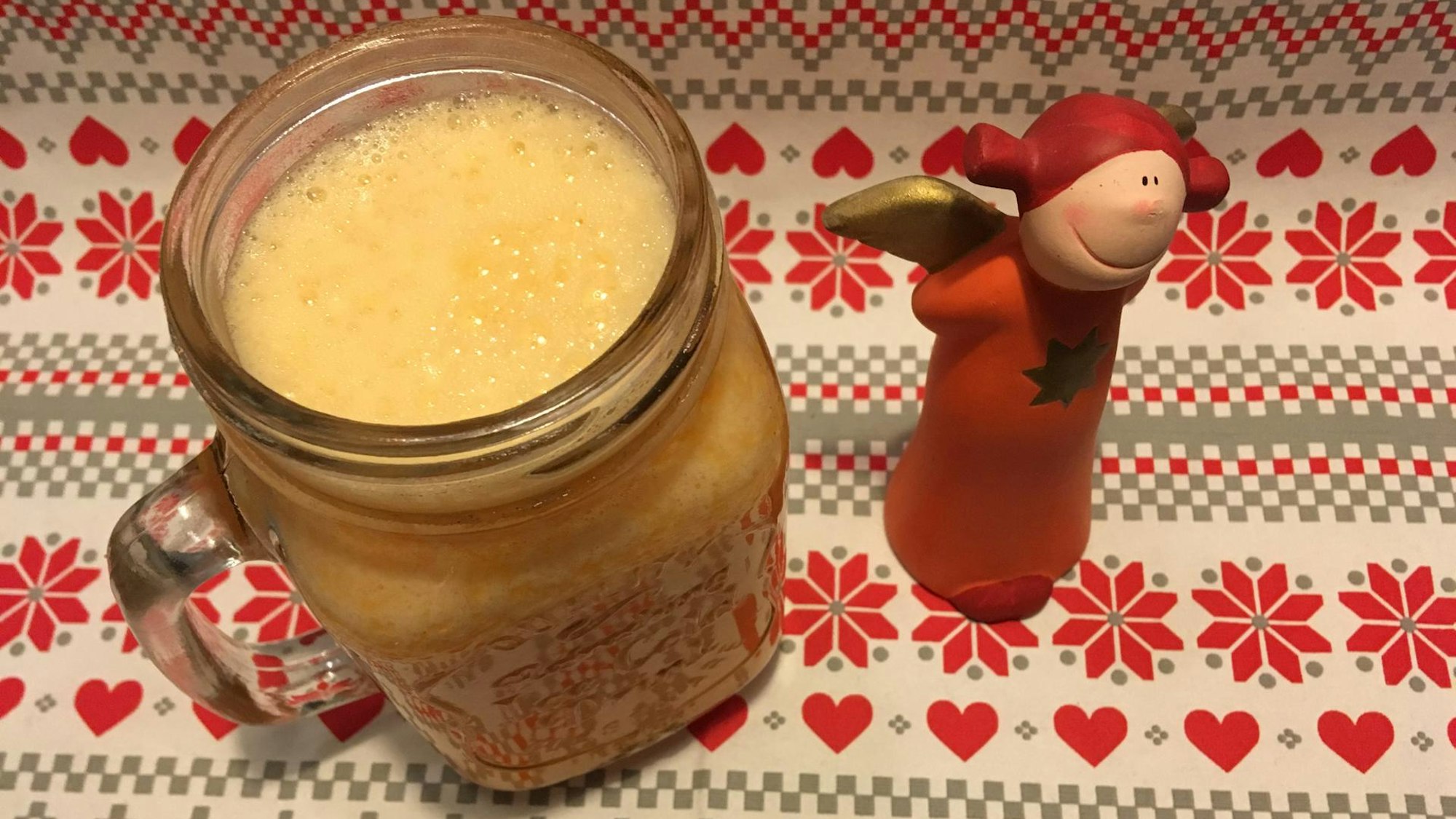 Orangen-Möhren-Smoothie in einem Glas, daneben ein roter Deko-Engel