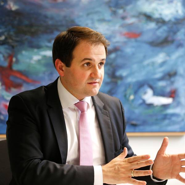 NRW-Europaminister Nathanael Liminski (CDU) in einer Gesprächssituation, den Gesprächspartner sieht man nicht. Er sitzt vor einem großen abstrakten Gemälde mit viel Blau, trägt einen dunklen Anzug, weißes Hemd und rosafarbene Krawatte.