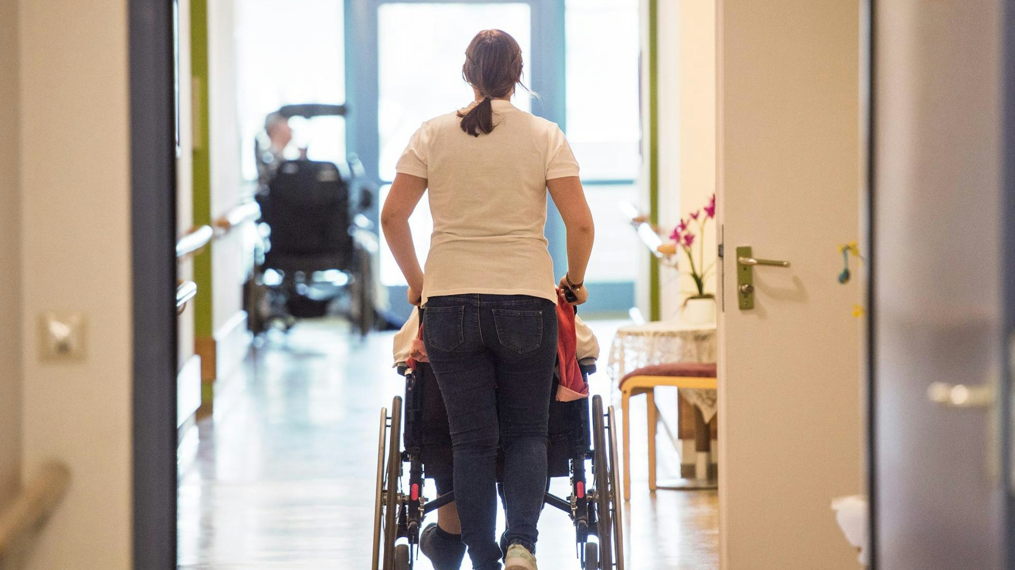 Eine Pflegerin schiebt eine Heimbewohnerin, die im Rollstuhl sitzt.