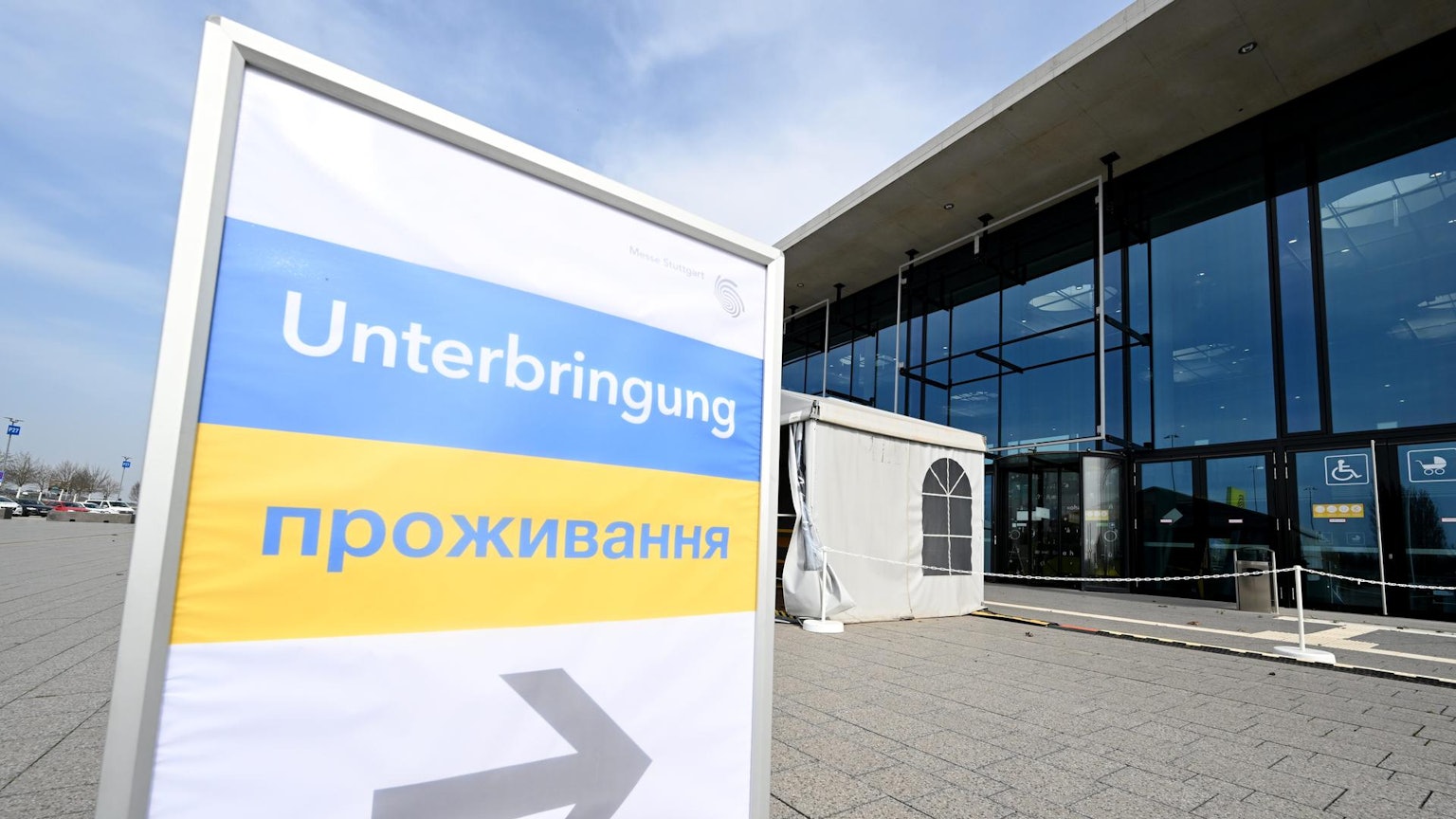 Ein Schilt mit ukrainischer Flagge und der Aufschrift Unterbringung zeigt auf ein Glasgebäude.