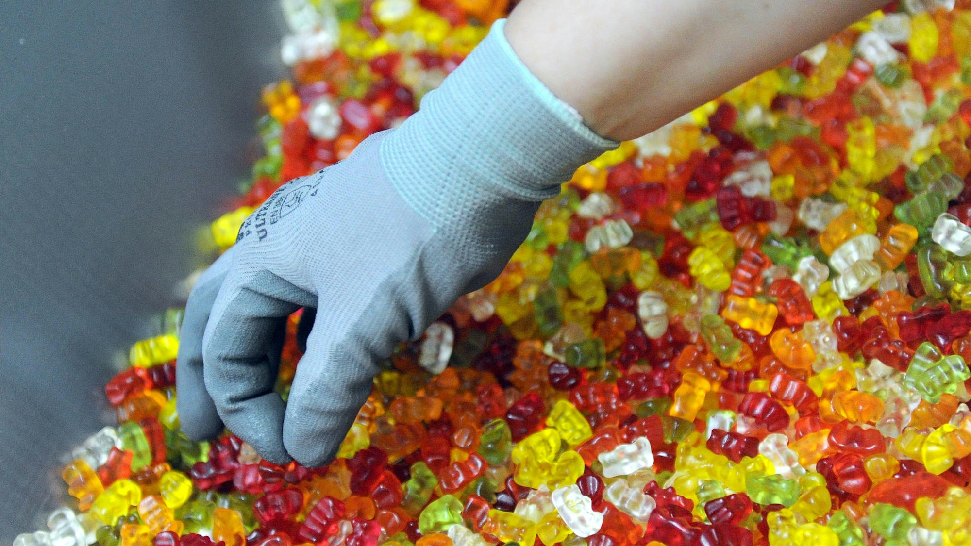 Hand mit Handschuh greift in eine große Menge Gummibärchen