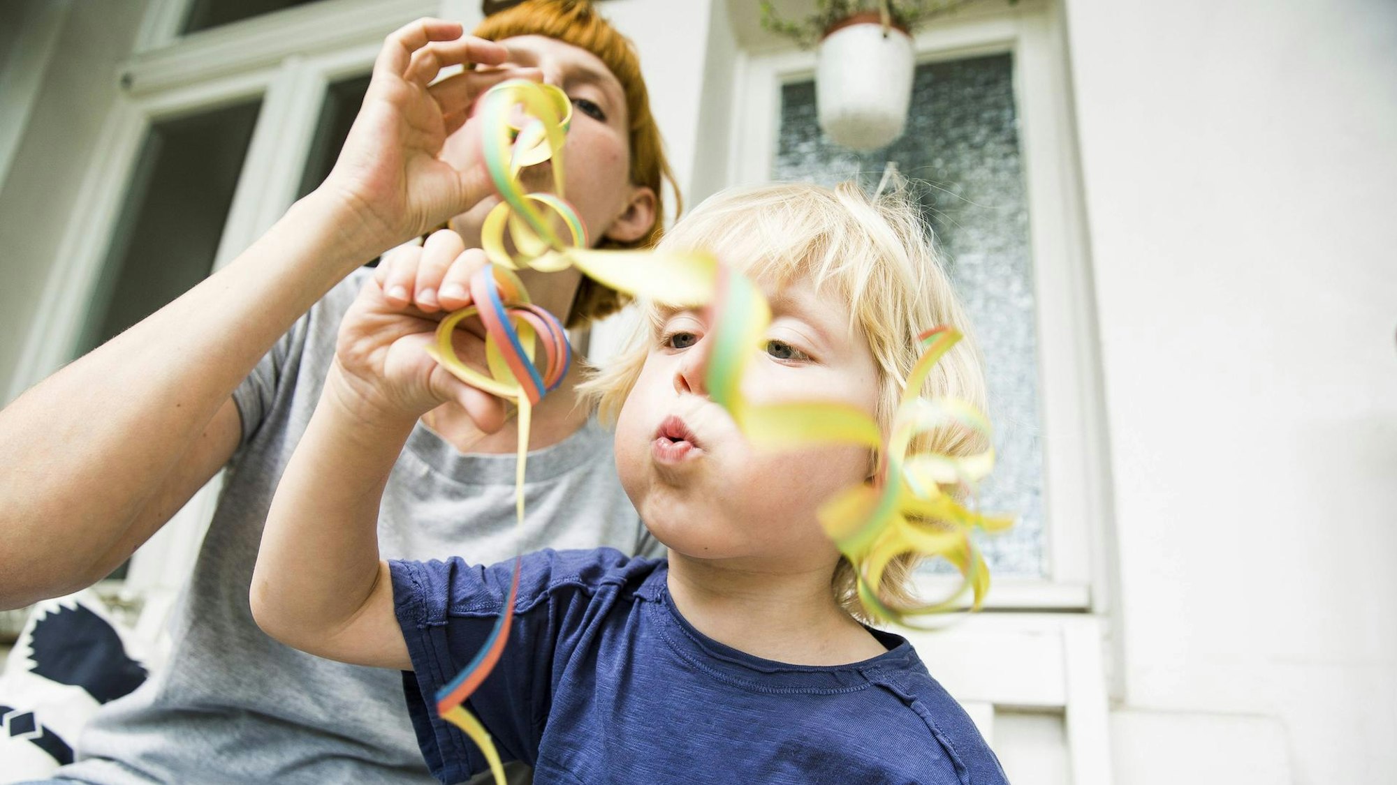 Eine Mutter und ihr Kind blasen Luftschlangen aus.