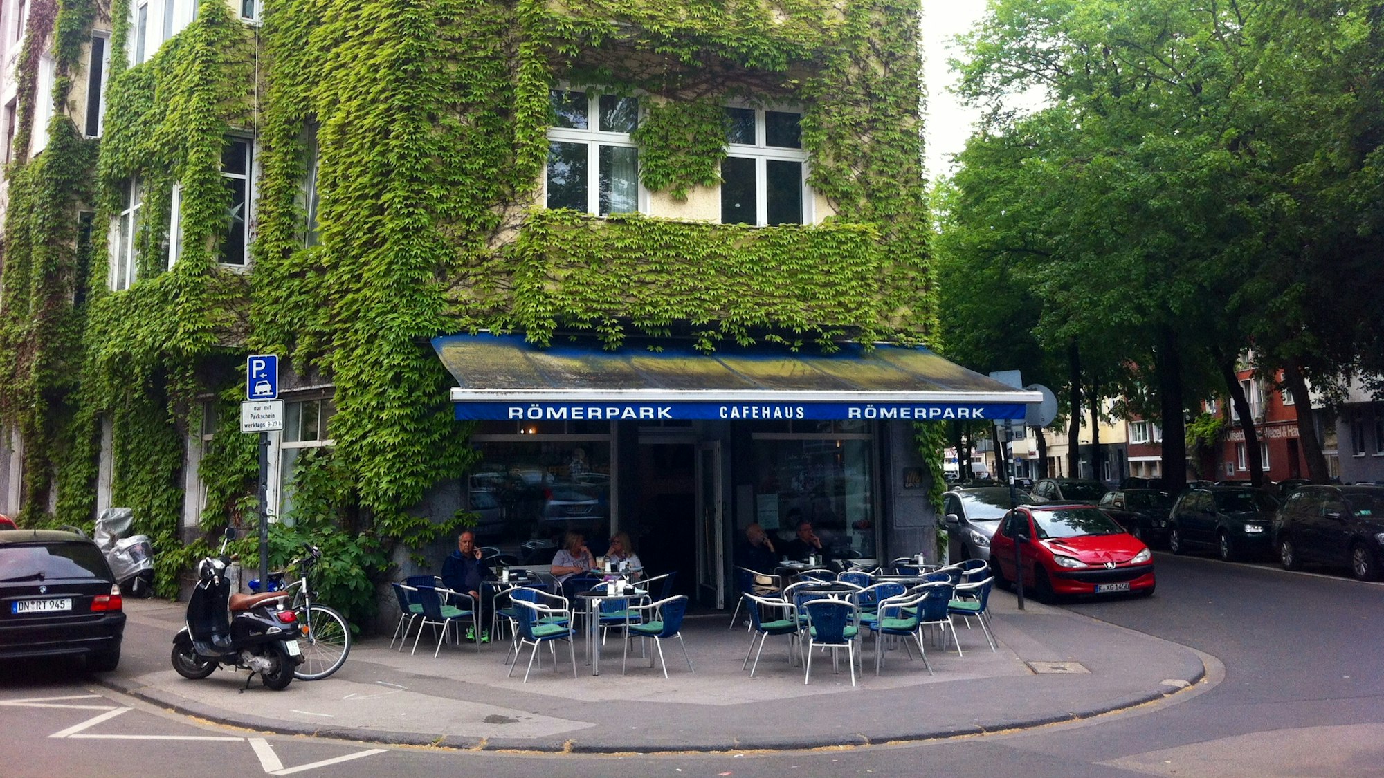 grün bewachsenen Haus an einer Straßenecke, vor dem Tische und Stühle stehen