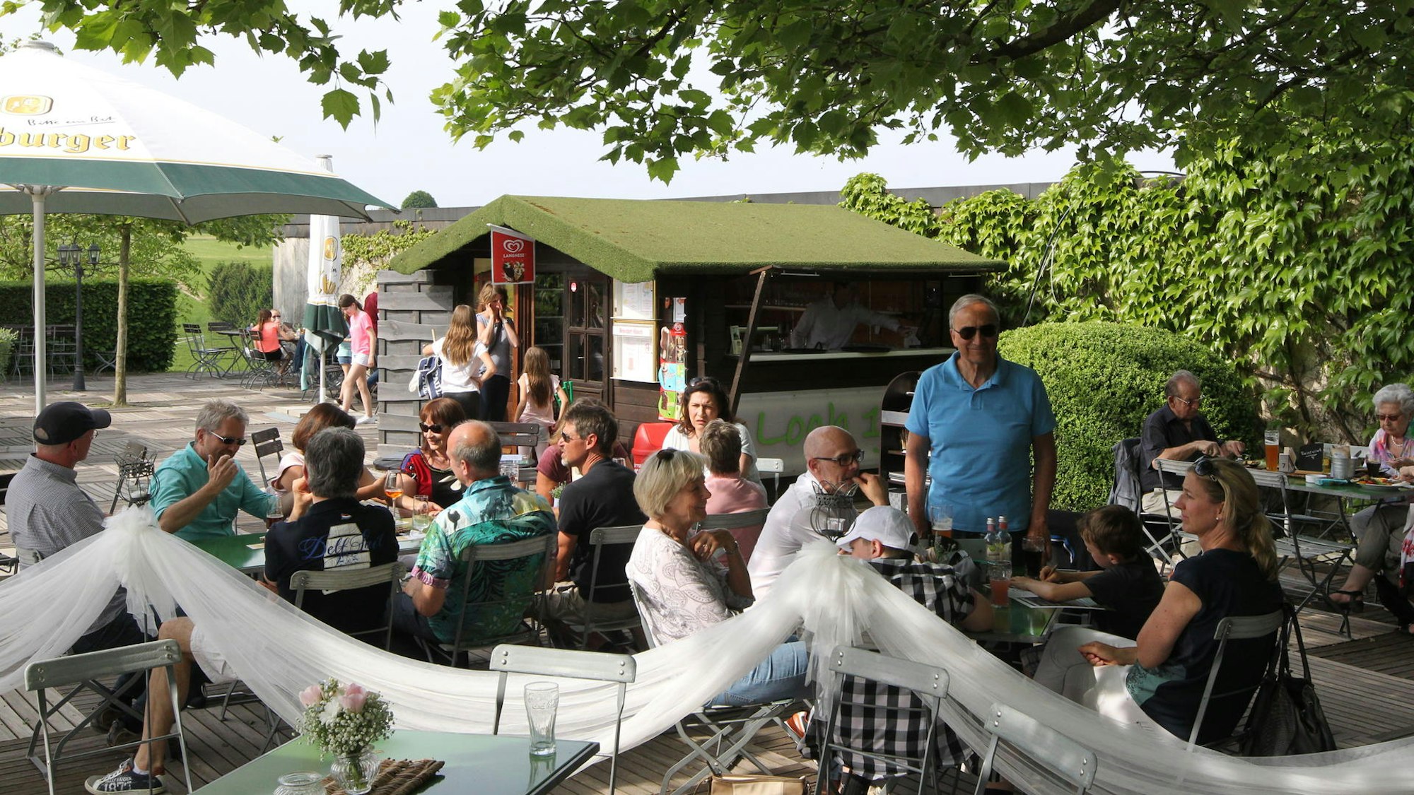 Schattig unter einem Baum sitzen mehrere Personen an Tischen.