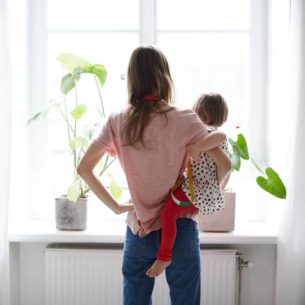 Eine Frau mit Kleinkind auf dem Arm schaut zum Fenster hinaus.