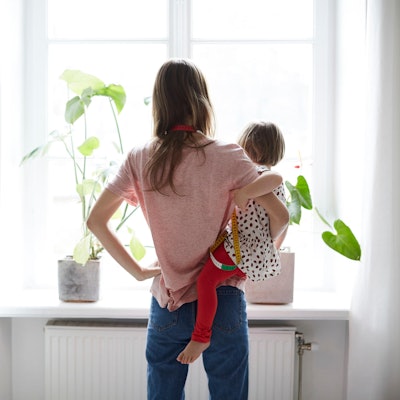 Eine Frau mit Kleinkind auf dem Arm schaut zum Fenster hinaus.