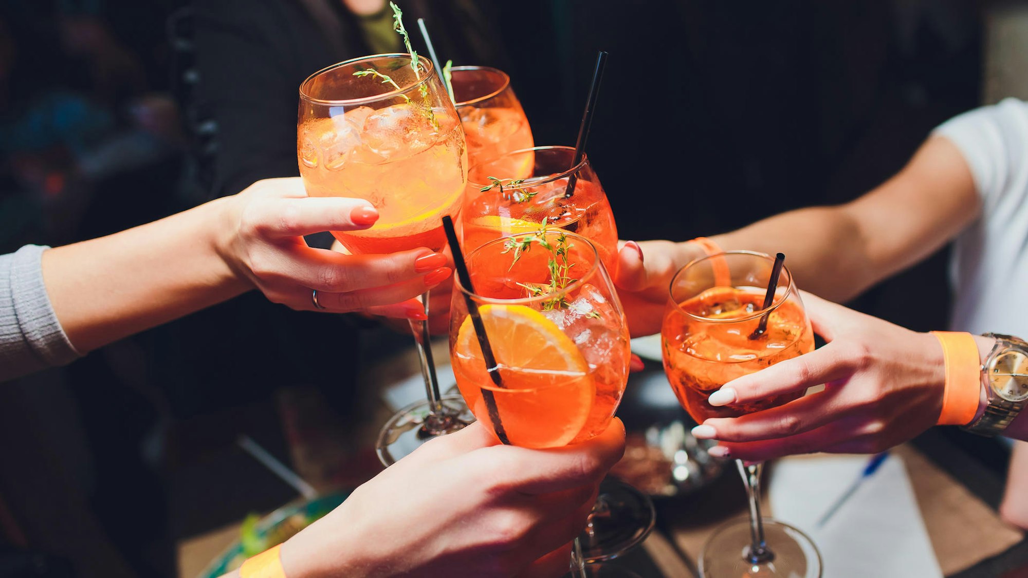 Menschen stoßen mit Gläsern an, in denen Aperol ist.