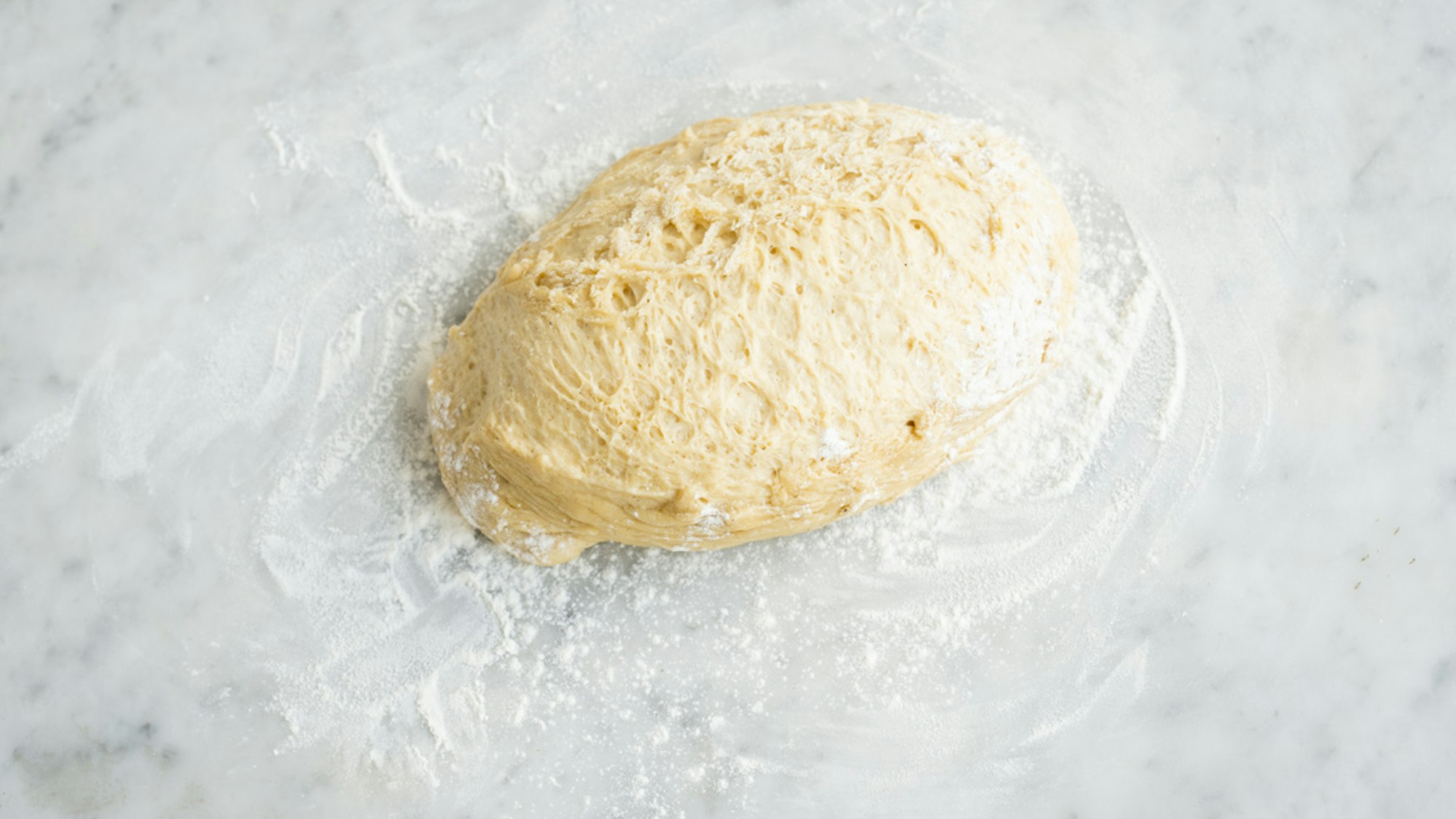 Ein Haufen Hefeteig liegt in Mehl auf einer Arbeitsplatte.