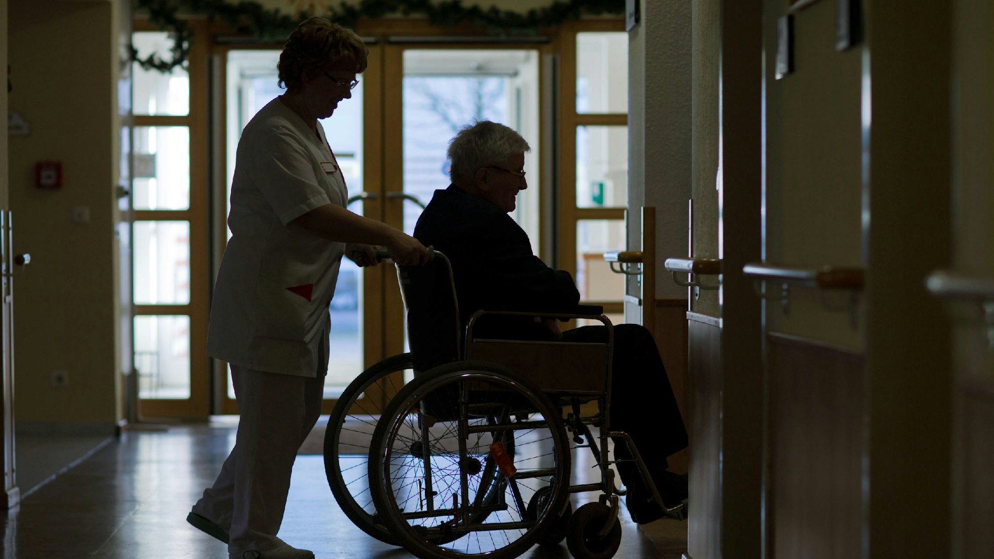 Eine Pflegerin schiebt einen älteren Mann im Rollstuhl.