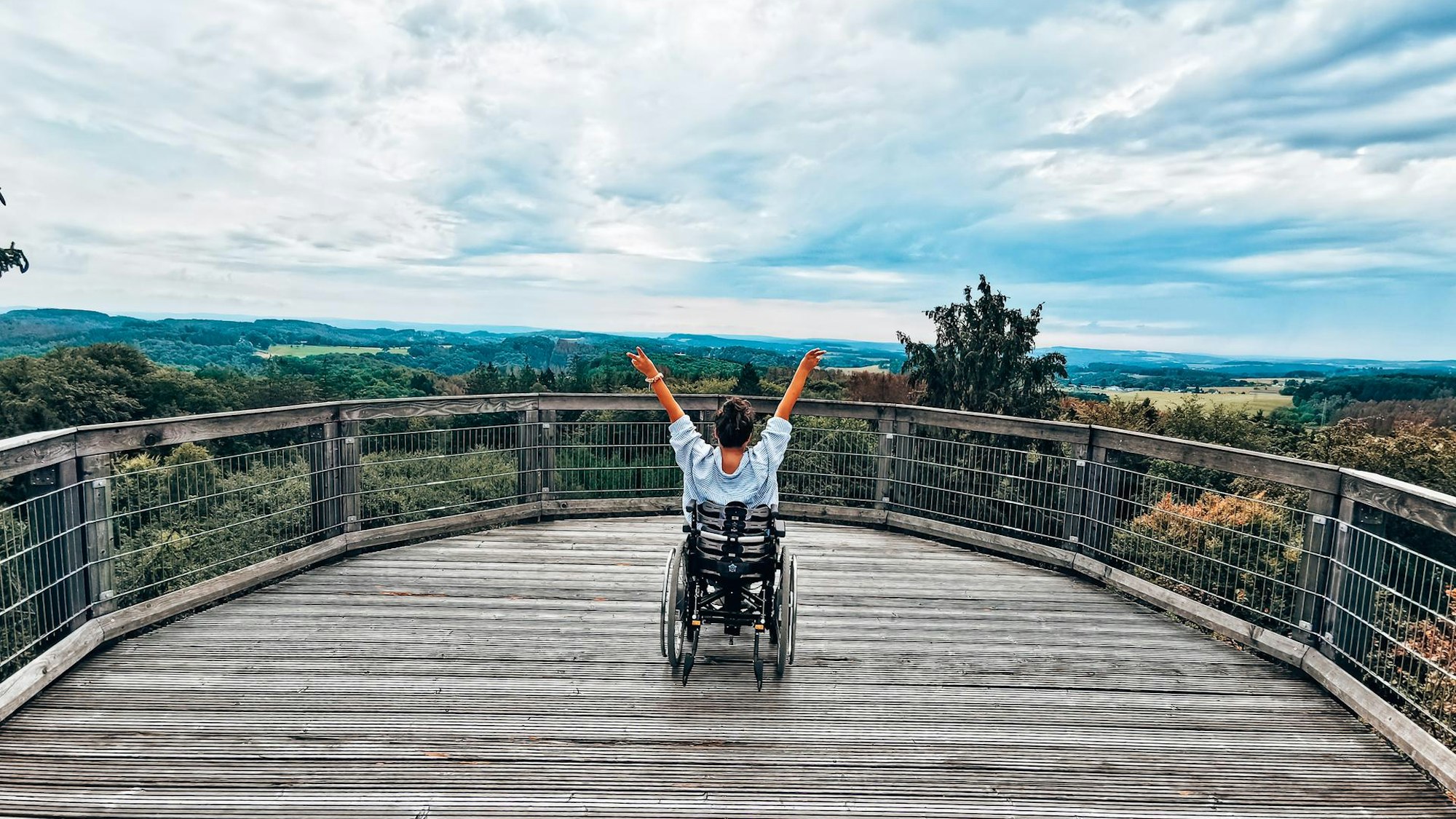 Eine Rollstuhlfahrerin auf einer Aussichtsplattform des Baumwipfelpfads Panarbora in Wadbröl.