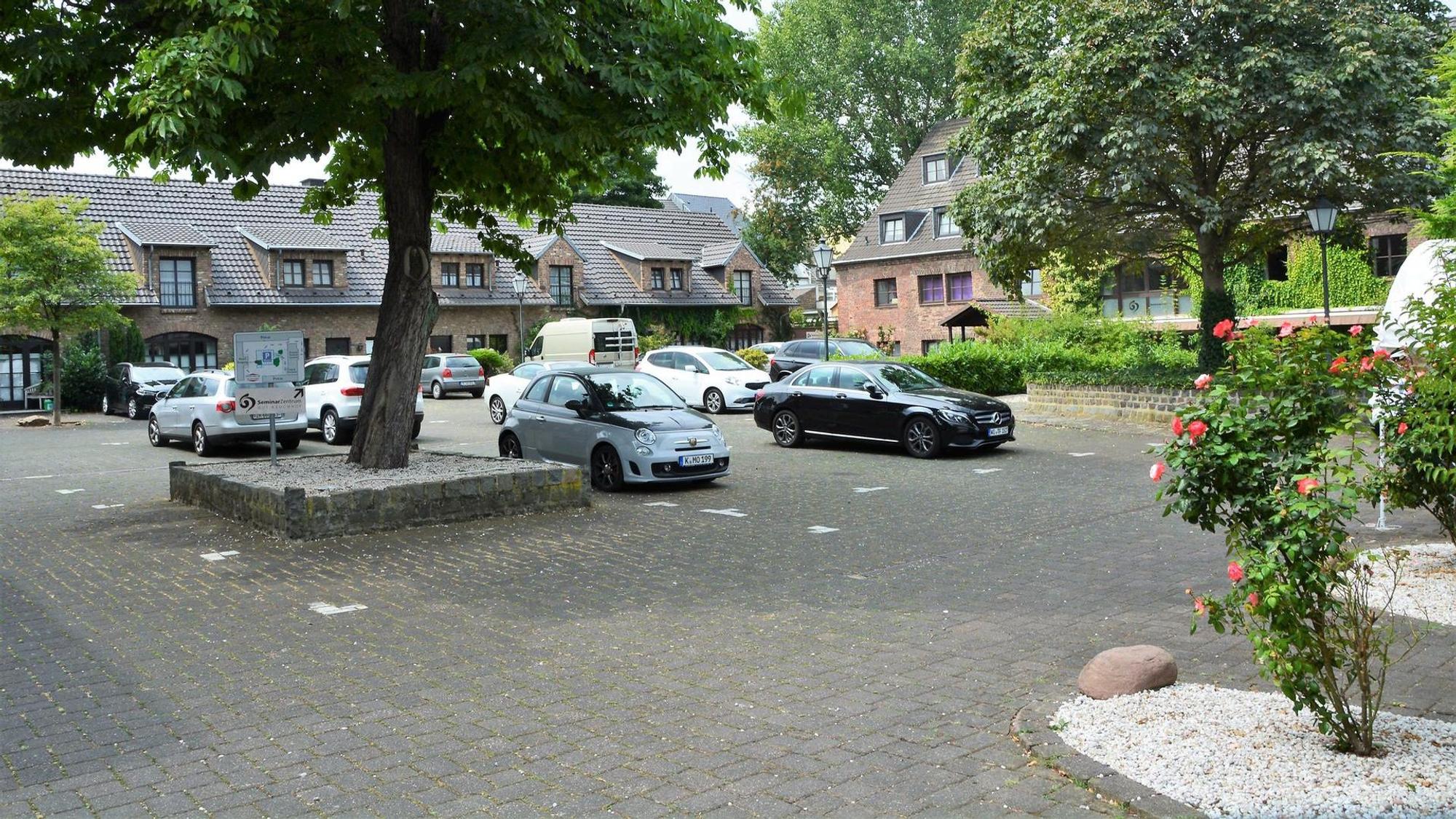 Ein gepflasterter Platz mit einigen eingefassten Bäumen und daneben geparkte Autos.